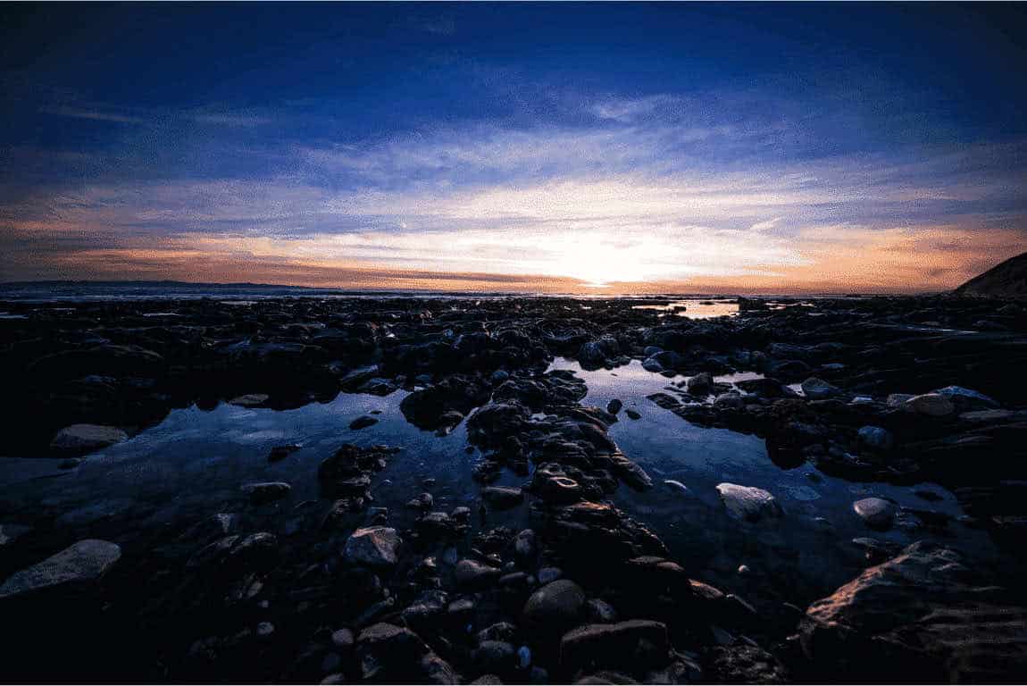 The sun sets over a rocky beach