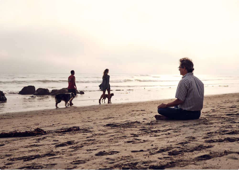 Man sitting on a beach meditating as the sun goes down